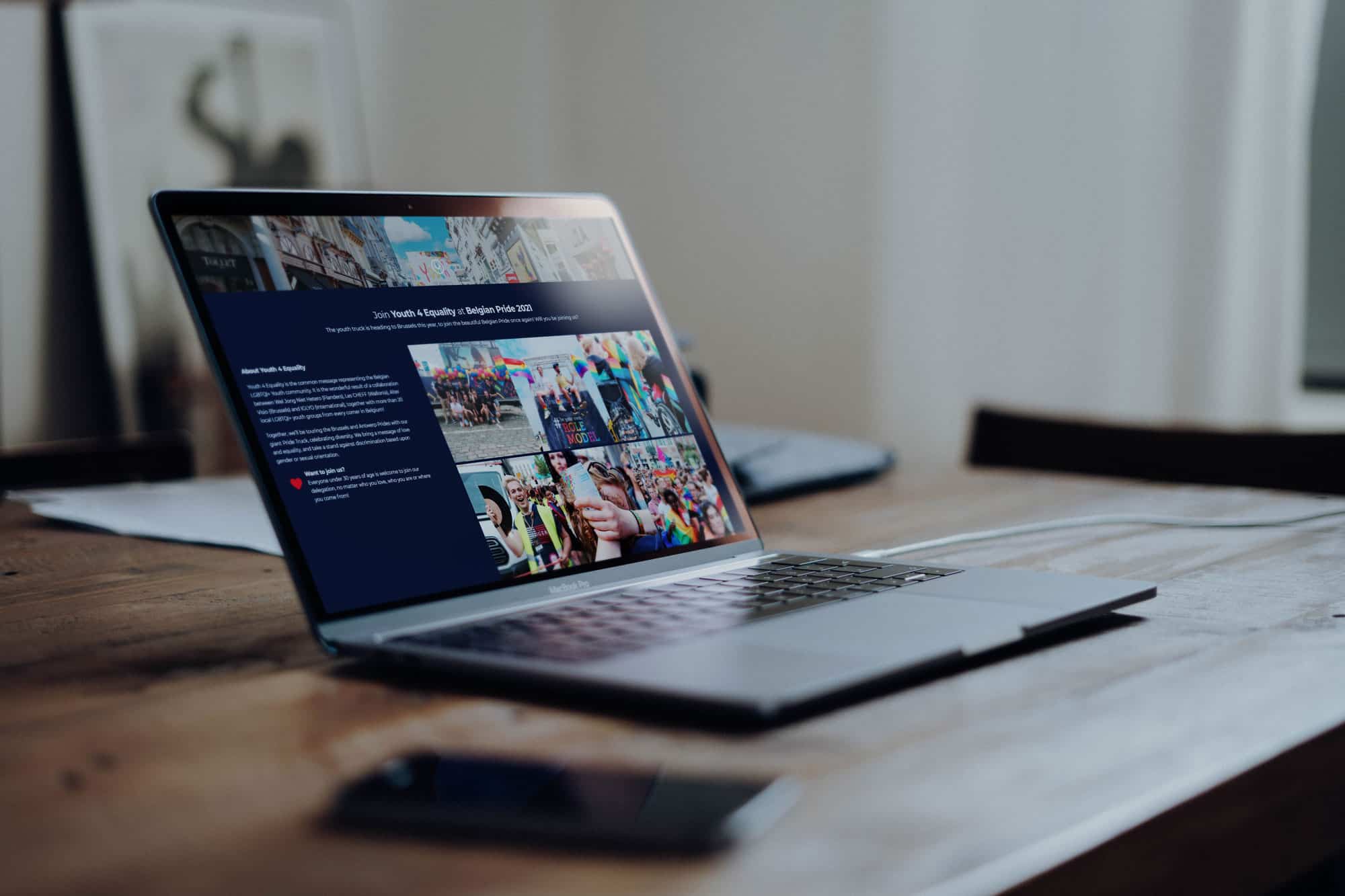 Laptop op een houten tafel toont een webpagina van Youth 4 Equality over hun deelname aan Belgian Pride 2020, met foto's die de energie en diversiteit van het evenement weerspiegelen.